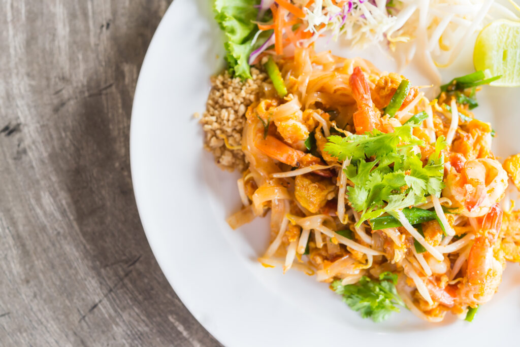 A plate of food, featuring a delicious Pad Thai recipe, sits on a wood table.