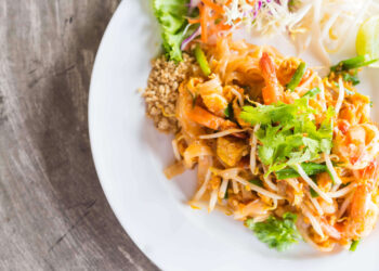 A plate of food, featuring a delicious Pad Thai recipe, sits on a wood table.