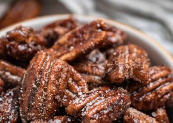 Close-up of a bowl filled with citrus maple candied pecans sprinkled with sugar, showcasing their glossy, textured surfaces and rich brown color.