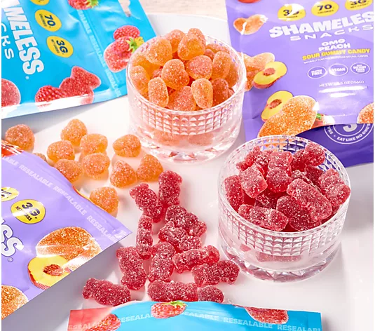 Glass cups and resealable bags filled with peach and red sour gummy candies are arranged on a white surface. Some gummies are scattered outside the cups and bags. The pastel blue and purple packaging highlights fiber benefits for seniors, making these colorful treats both tasty and supportive of healthy aging.