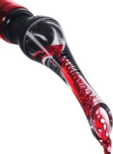 Close-up of red wine being poured through a clear wine aerator, one of the essential wine tools for wine lovers, attached to the neck of a bottle, with wine visibly swirling inside the aerator against a white background.
