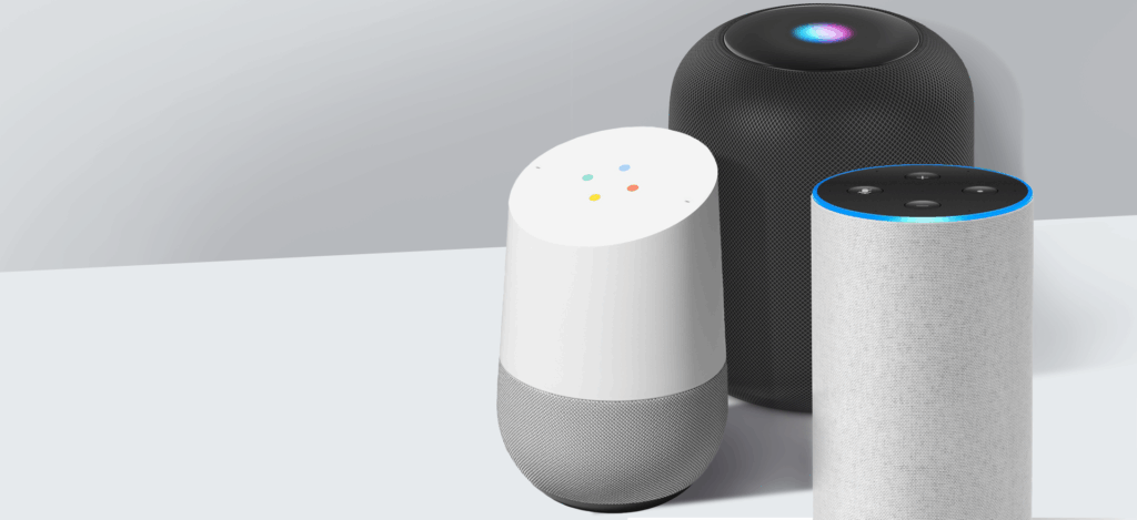 Three smart speakers are displayed on a white surface, showcasing ideal smart home gadgets for seniors: a white and gray Google Home, a tall gray Amazon Echo with a blue light ring, and a black cylindrical speaker with a glowing blue light on top.