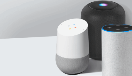 Three smart speakers are displayed on a white surface, showcasing ideal smart home gadgets for seniors: a white and gray Google Home, a tall gray Amazon Echo with a blue light ring, and a black cylindrical speaker with a glowing blue light on top.
