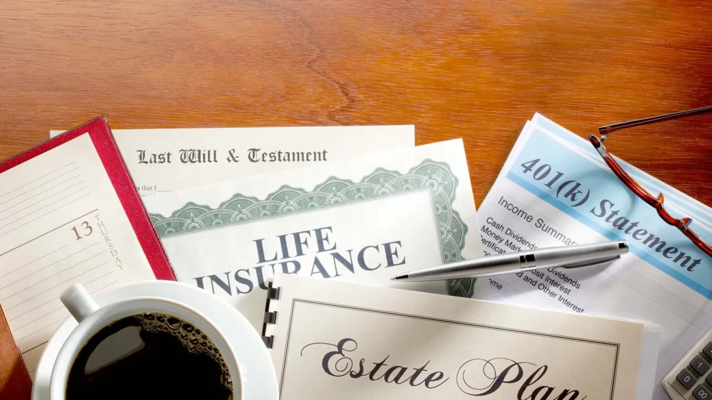 A table with documents including a last will and testament, life insurance policy, estate plan, and 401(k) statement. A pen, reading glasses, a planner, and a cup of coffee are also visible.