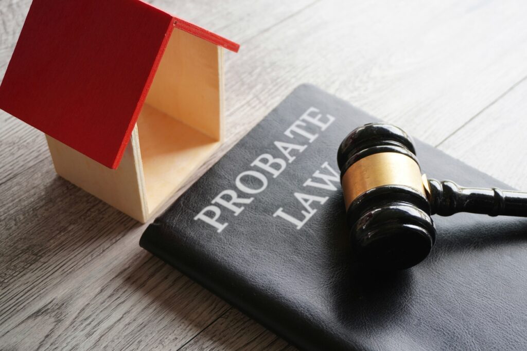 A wooden model house, a judge’s gavel, and a black book labeled PROBATE LAW rest on a wooden surface, symbolizing legal issues related to property inheritance.