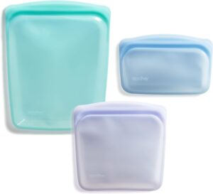 Three reusable silicone storage bags in light aqua, blue, and lavender colors are displayed on a white background. The bags are of different sizes and feature a rounded rectangular shape with a seal at the top.