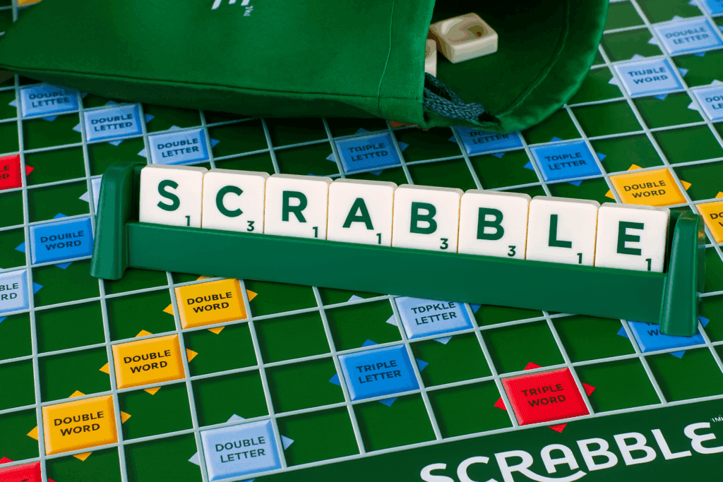 A Scrabble game board with a tile rack holding letter tiles that spell SCRABBLE. The board shows premium score squares, a green tile bag in the background, highlighting the mental benefits of Scrabble for seniors.