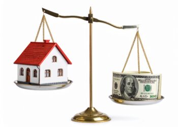 A brass balance scale with a small house model on one side and a stack of U.S. hundred dollar bills on the other, highlighting things that hurt your home’s value by comparing real estate worth to cash.