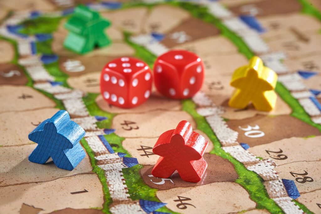 Four colorful wooden game pieces and two red dice are placed on a numbered board game map with winding paths, blue, green, and brown terrain—perfect for fun board games for kids.