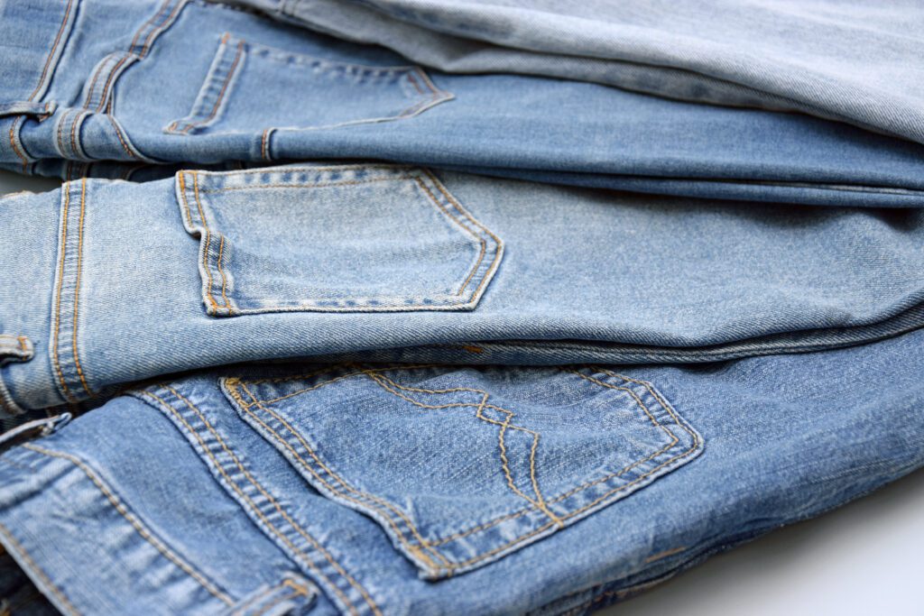 Three pairs of blue jeans in different shades of denim are stacked on top of each other, showing the back pockets and seams—perfect for those seeking the best jeans for women over 50.