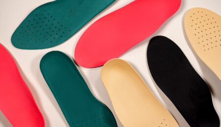 Several colorful shoe insoles, ideal as orthotics for seniors, are arranged on a light background. Available in green, red, beige, and black, some feature small perforated holes and vary slightly in shape and size.