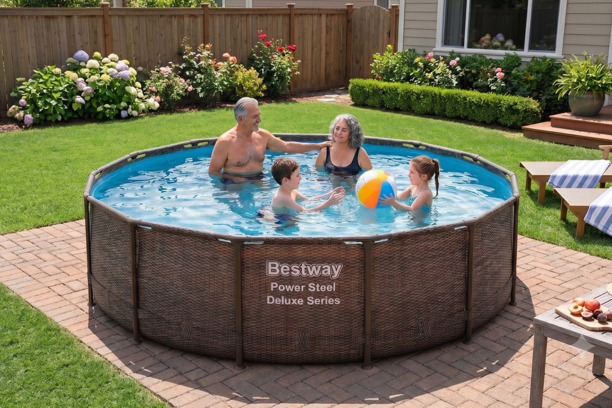 Two adults and two kids play with a beach ball in a round above-ground pool in a backyard garden. Bestway Power Steel Deluxe Series is written on the pool’s side, showcasing one of the best backyard pools for family fun. Lawn chairs and flowers are visible in the background, enhancing the inviting outdoor setting.