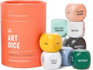 A cylindrical orange container labeled Art Dice sits next to nine colorful dice, each with different art prompts such as LOVE, STILL LIFE/PORTRAIT, REPTILE, and ABSTRACT.