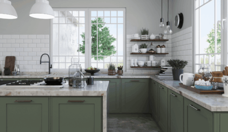 Bright, modern kitchen with green cabinets, white subway tile backsplash, marble countertops, large windows, open shelves with dishes and plants, and pendant lights hanging from the ceiling.