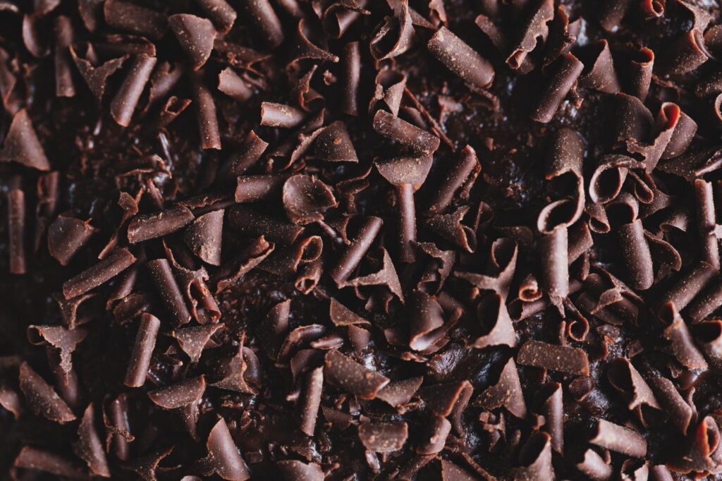 Close-up of dark chocolate shavings scattered across a surface, reminiscent of ingredients used in a dark chocolate bark recipe, creating a rich and textured appearance.