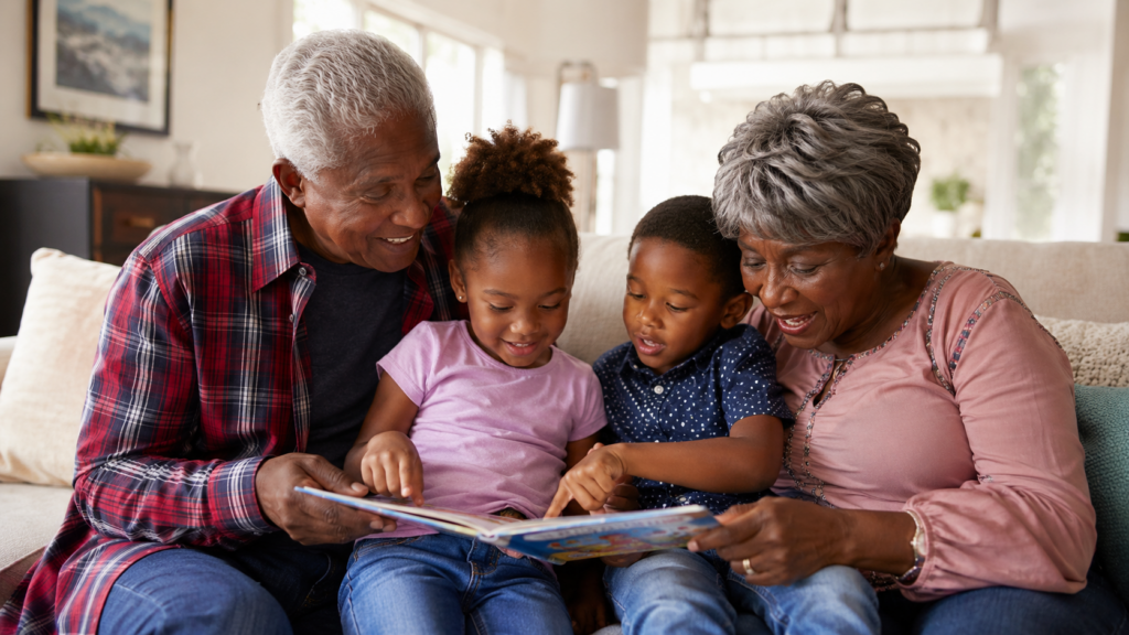 Two grandparents sit on a sofa with their two young grandchildren, smiling and reading a book together in a bright, cozy living room—a perfect example of family joy that comes from setting boundaries with adult kids.