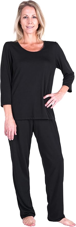 A woman with blonde hair, smiling, stands barefoot in a black long-sleeve pajama set—one of the menopause must haves—featuring loose-fitting pants and a round-neck top against a white background.