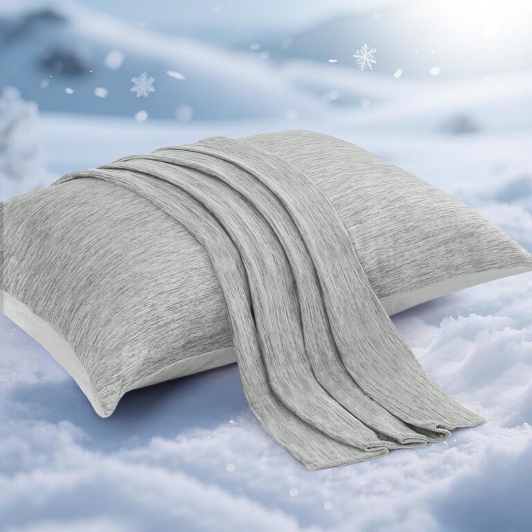 A soft gray scarf—one of the menopause must haves—draped over a matching pillow, both resting on snow with a wintry background featuring gentle snowflakes and blurred snowy scenery.