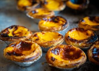 Close-up of several Portuguese custard tarts (pastéis de nata) with golden, caramelized tops and flaky pastry crusts, arranged on a baking tray.