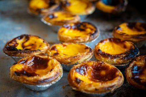Close-up of several Portuguese custard tarts (pastéis de nata) with golden, caramelized tops and flaky pastry crusts, arranged on a baking tray.