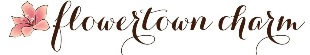 Logo with the words flowertown charm in elegant, brown cursive script, featuring a pink flower illustration to the left of the text.